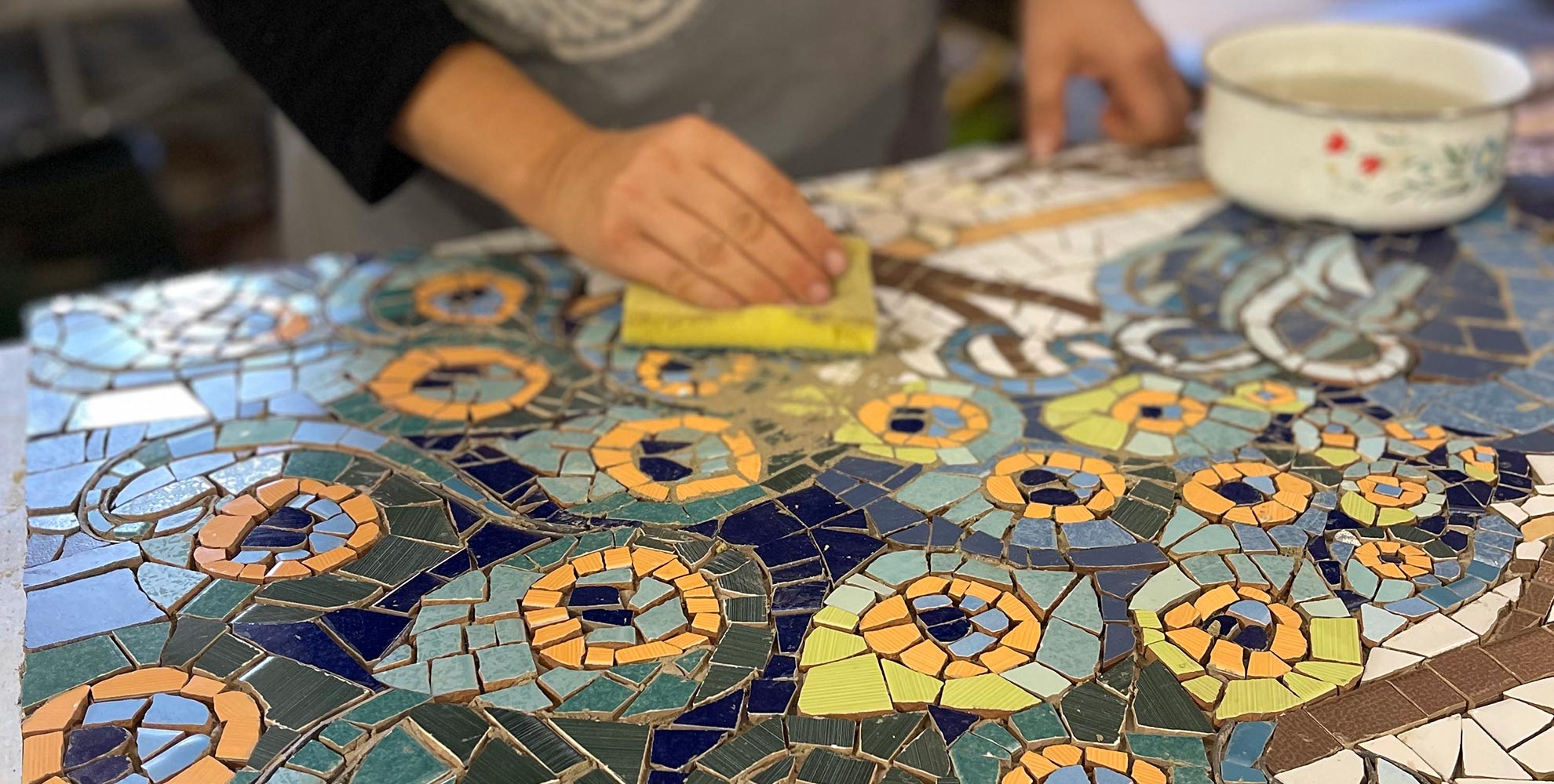 mosaicista che lavora alla creazione di un mosaico a trencadis che rappresenta un pavone colorato sui toni del azzurro e ocra